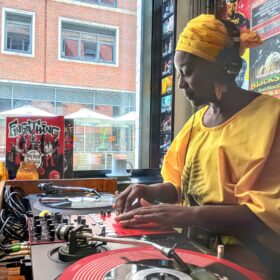 A woman wearing yellow clothes with her hands on a DJ mixing deck.