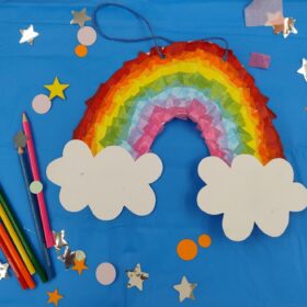 A paper rainbow, star-shaped stickers and some coloured pencils lying on a blue table.