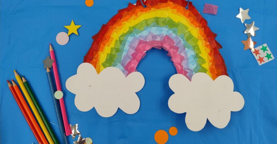 A paper rainbow, star-shaped stickers and some coloured pencils lying on a blue table.