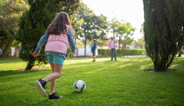 A girl with a football at her feet on a grassy pitch.