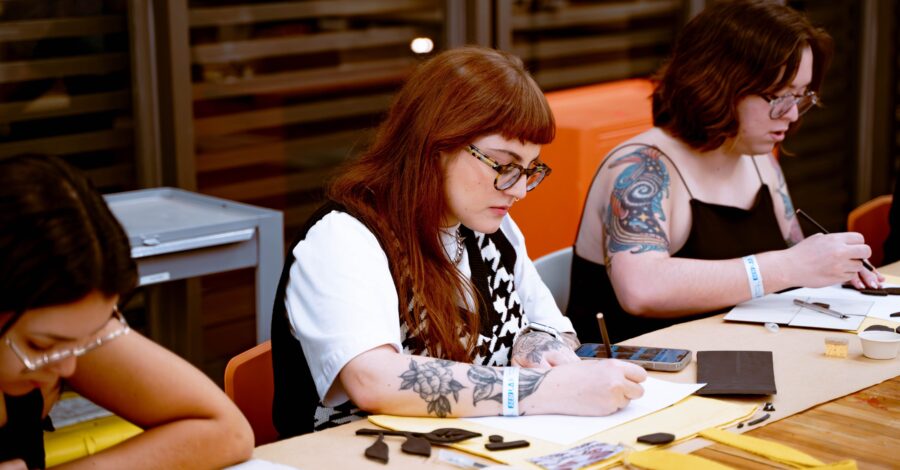 Three people sat at a table writing on a pad with a pen.
