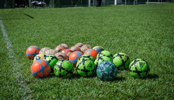 A range of different coloured footballs on a sports field.