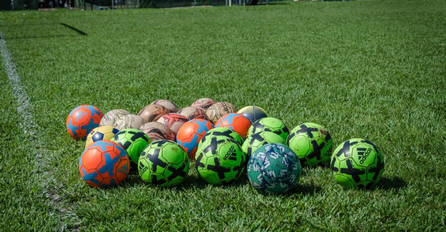 A range of different coloured footballs on a sports field.