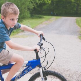 A boy riding a blue bike on a graveled path.