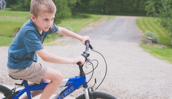 A boy riding a blue bike on a graveled path.