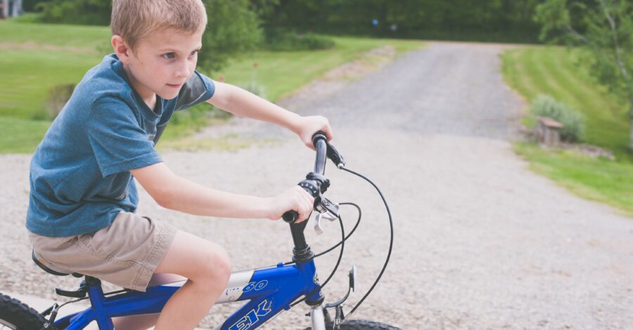 A boy riding a blue bike on a graveled path.