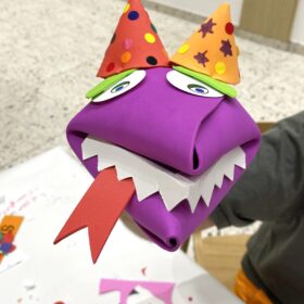A purple hand crafted puppet made out of paper.