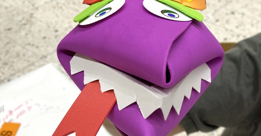 A purple hand crafted puppet made out of paper.